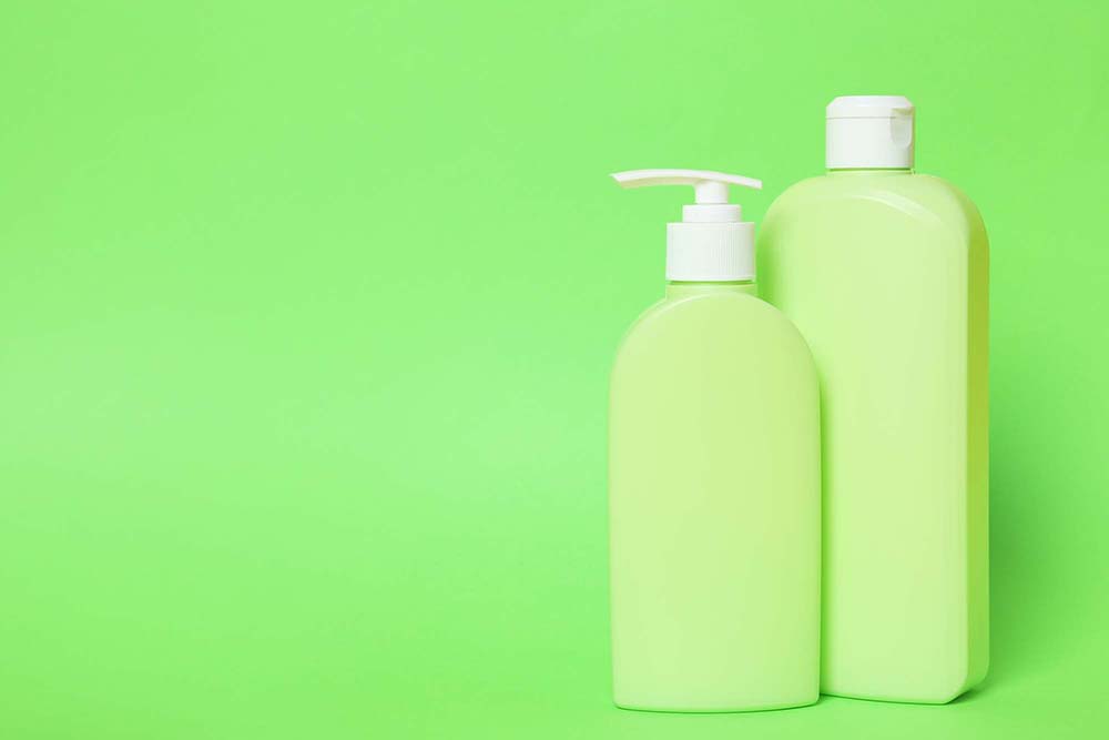 Bottles of shampoo on green background, space for text. Natural